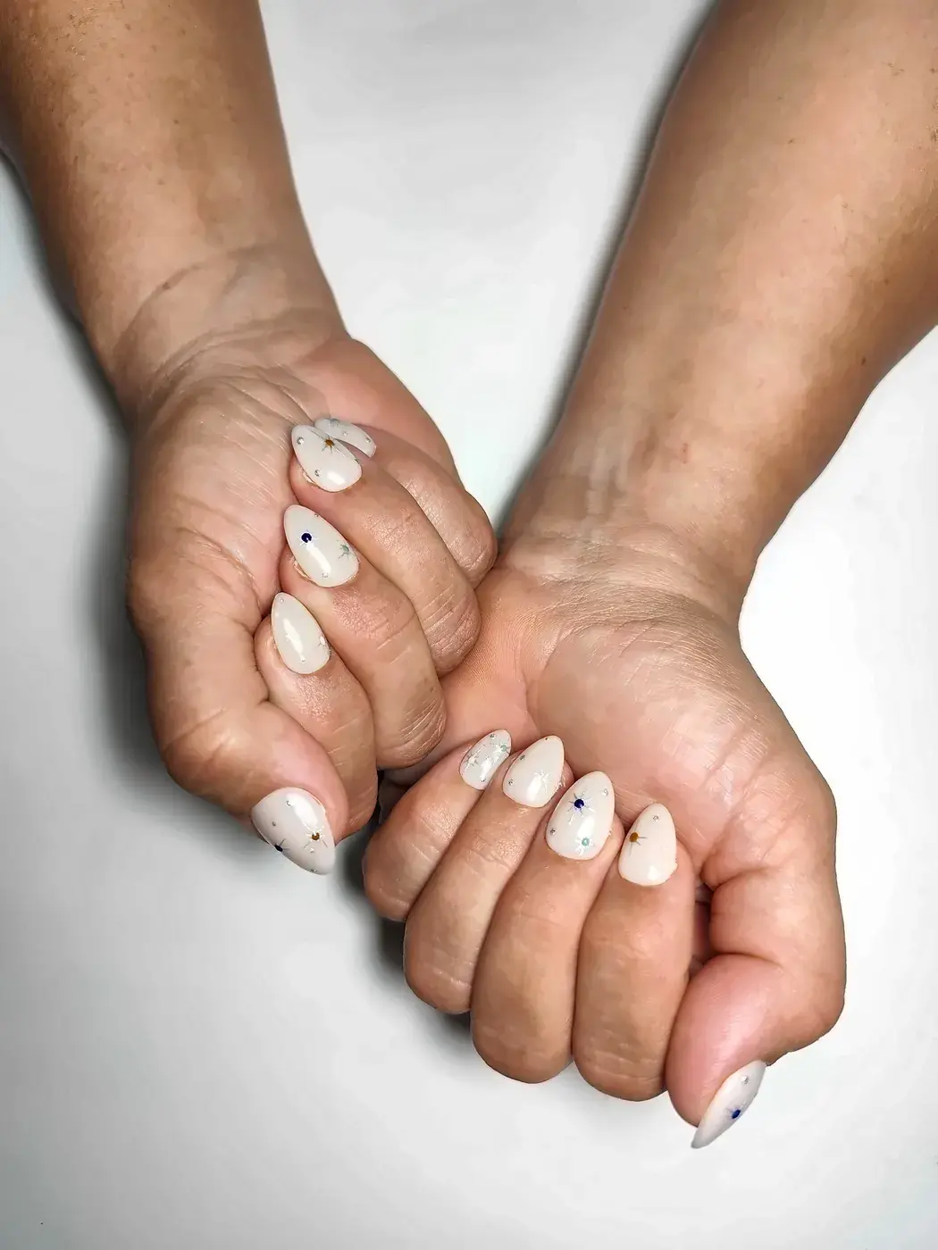 Manos juntas con uñas postizas almendra en blanco lechoso con estrellas plateadas
