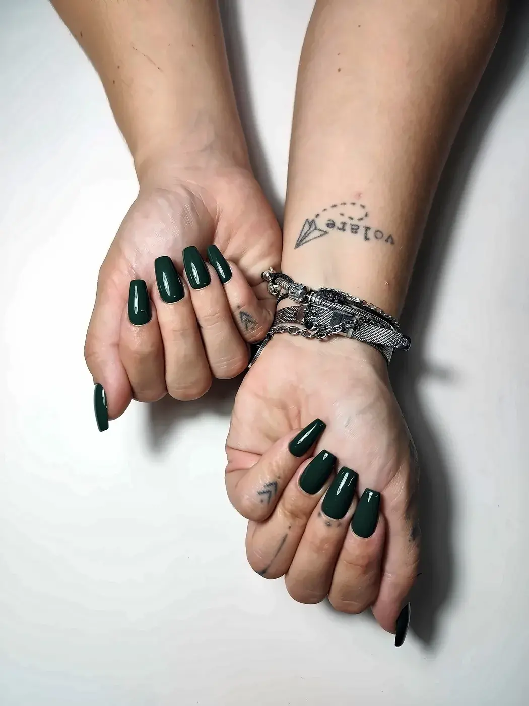 Manos juntas con uñas postizas coffin lisas en verde botella, con acabado brillante