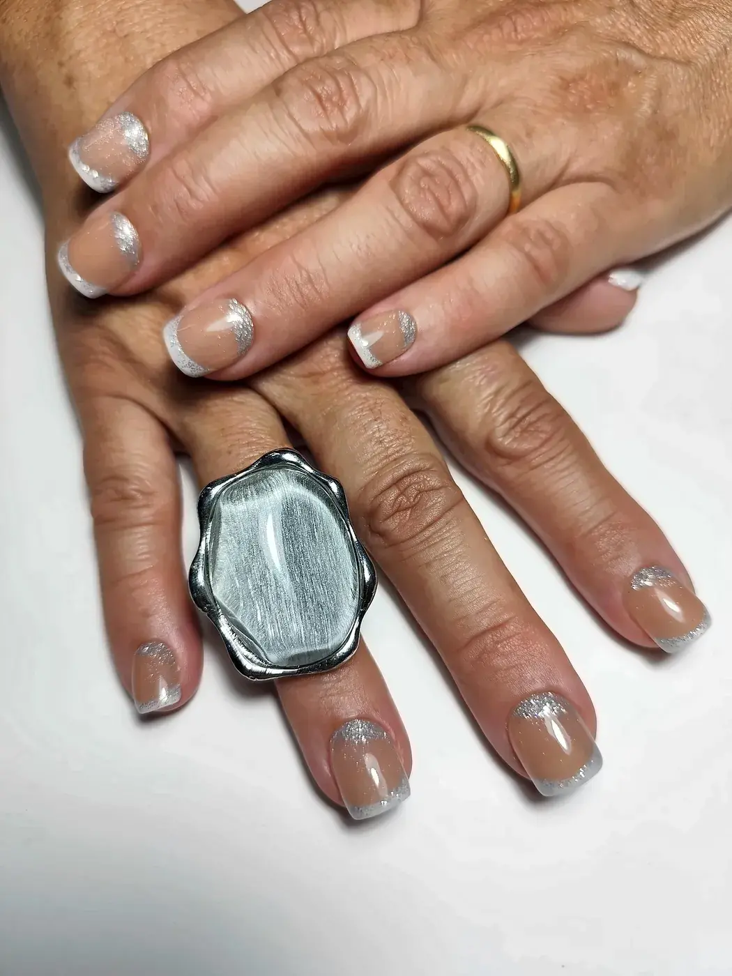 Manos una sobre otra con uñas postizas squoval cortas en nude caramelo con francesa plateada con purpurina
