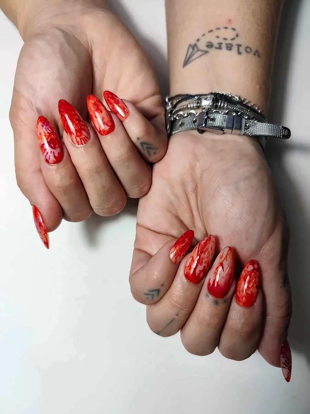 Dos manos con uñas postizas almendra largas en rojo acuarela con huellas de manos ensangrentadas