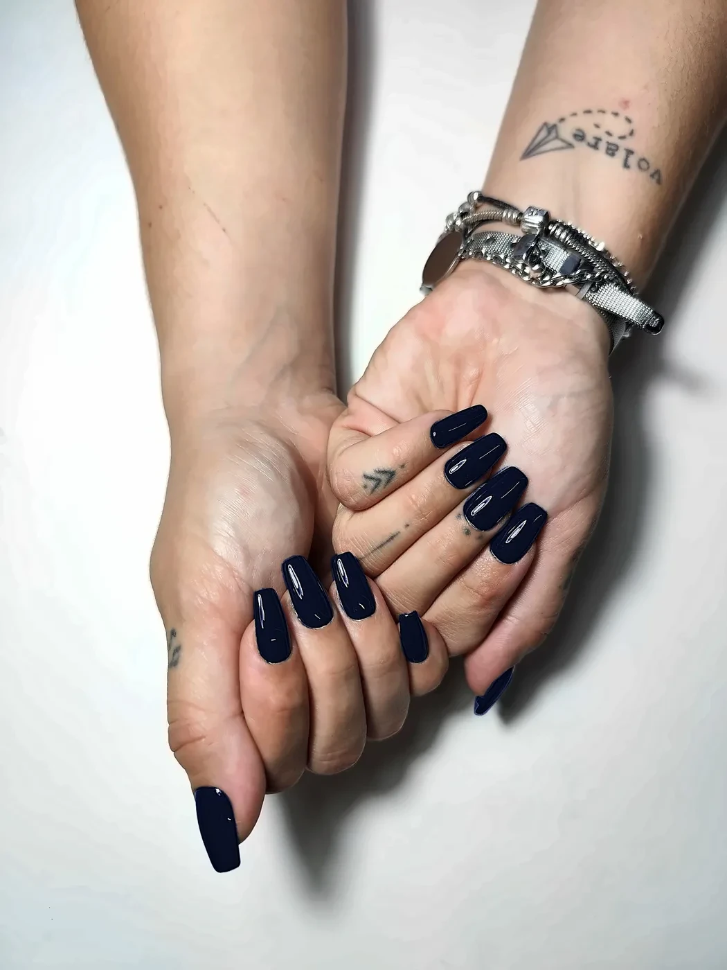 Manos juntas con uñas postizas coffin lisas en azul noche, con acabado brillante