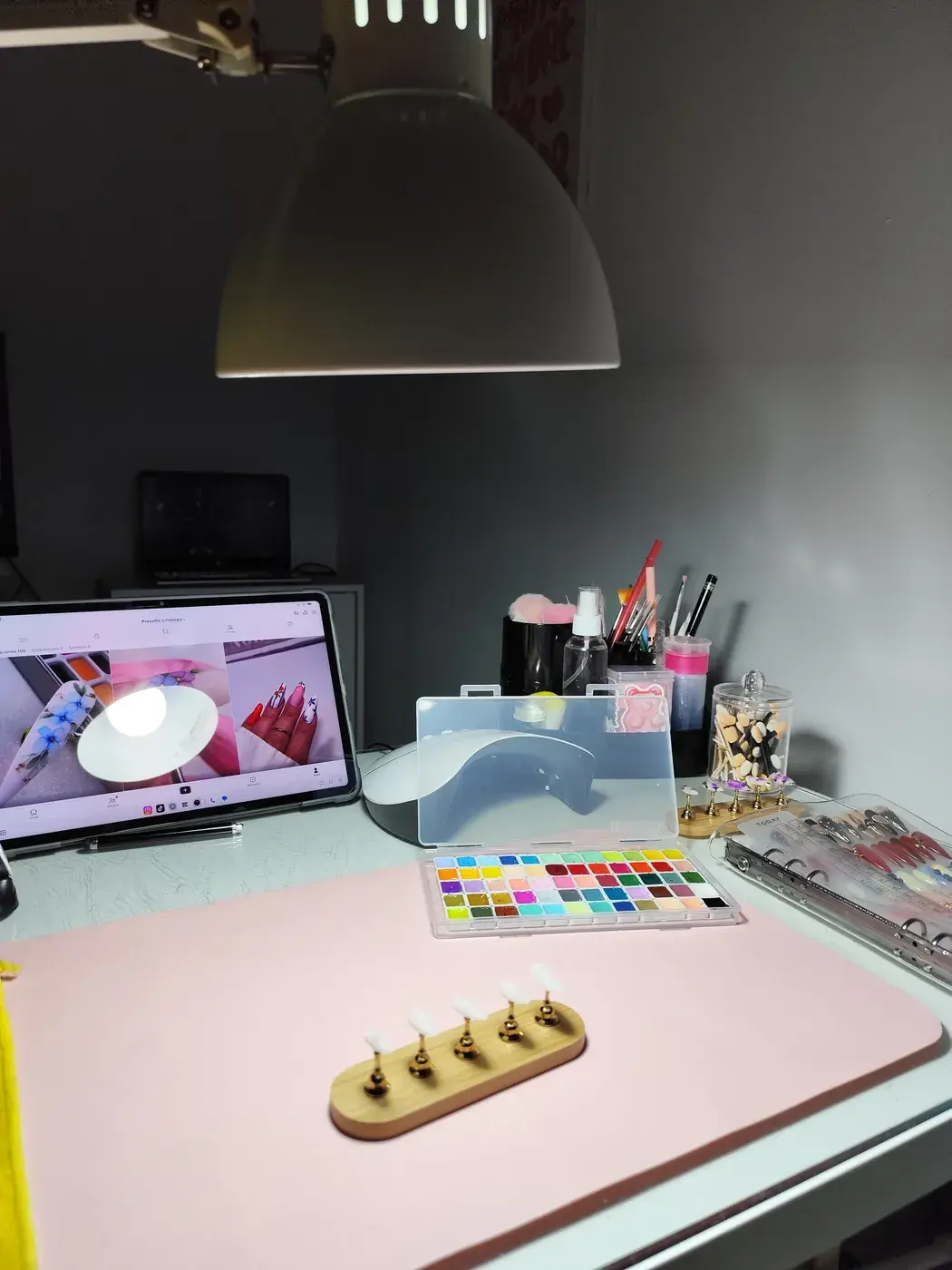 Mesa de trabajo de Cristina: alfombrilla rosa, lámpara de flexo, lámpara de secado, paleta de colores, soportes para uñas y pinceles