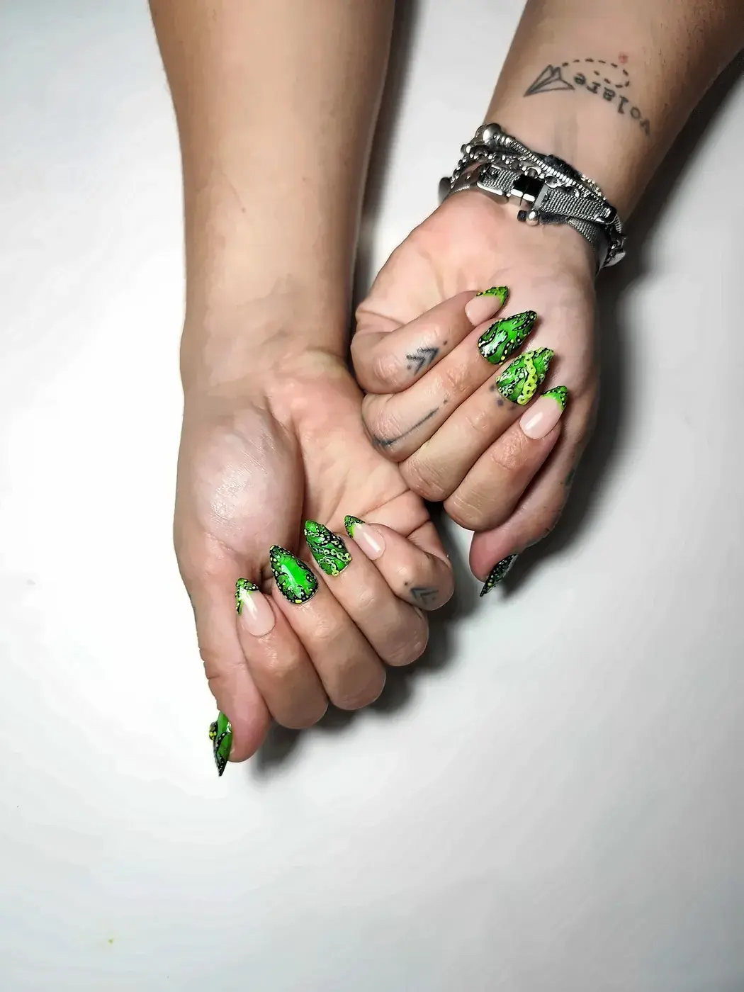 Manos con uñas postizas almendra en verde neón con tentáculos de pulpo pintados a mano en negro y amarillo, alternadas con francesas verdes