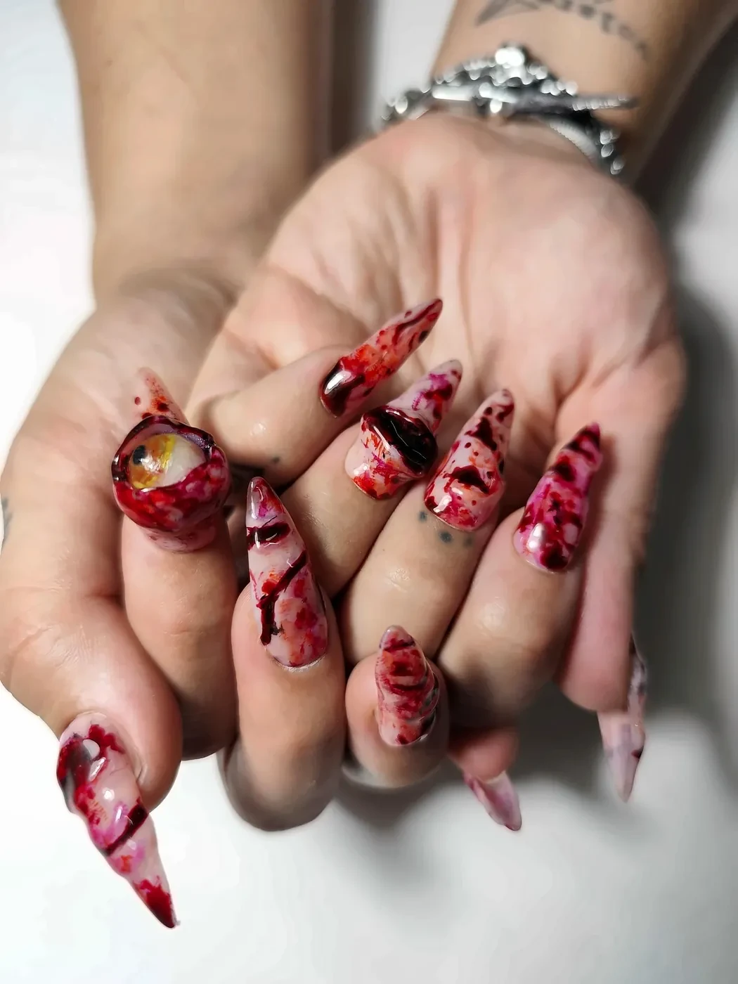 Manos con uñas postizas stiletto de Halloween con efecto sangre, heridas en relieve y un ojo 3D